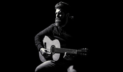 Bearded guitarist plays. Play the guitar. Beard hipster man sitting in a pub. Guitars and strings. Bearded man playing guitar, holding an acoustic guitar in his hands. Music concept. Black and white - obrazy, fototapety, plakaty