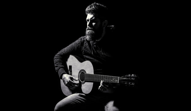 Bearded guitarist plays. Play the guitar. Beard hipster man sitting in a pub. Guitars and strings. Bearded man playing guitar, holding an acoustic guitar in his hands. Music concept. Black and white