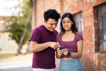 Young smiling couple on street using mobile.
