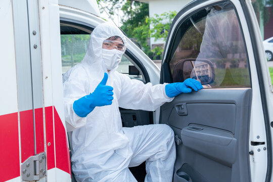 Happy Driver Wear PPE In Front Of The Ambulance With Protective Suit, Mask Gloves At Ambulance Car Vehicle For Helping The Patient Of Coronavirus Or Covid-19