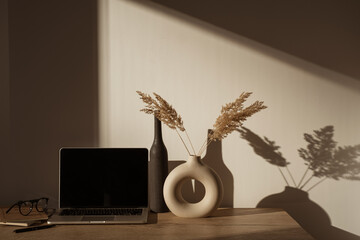 Laptop computer with blank screen on table with pampas grass bouquet in sunlight shadows on the...