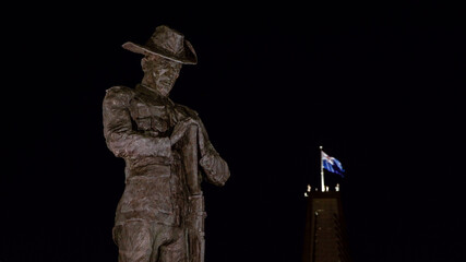 An ANZAC bronze cast statue near the ANZAC Bridge in Sydney looks down at night with a flag in the background.