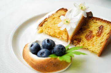 Easter yeast cake covered with icing and decorated with edible flowers and berries on a white plate, close-up.