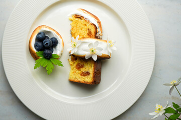  Easter yeast cake covered with icing and decorated with edible flowers and berries on a white plate, close-up.