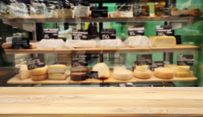 Naklejka na ściany i meble Mock up template, wooden table top, desk top counter in foreground for your product or text. Defocused blurred image of shelves with variety sorts of cheese. Farm craft view out of focus add template.