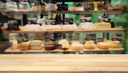 Mock up template, wooden table top, desk top counter in foreground for your product or text. Defocused blurred image of shelves with variety sorts of cheese. Farm craft view out of focus add template.