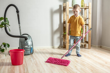 Little boy is cleaning the floor of a room using a mop. Concept of independence, help to parents,...