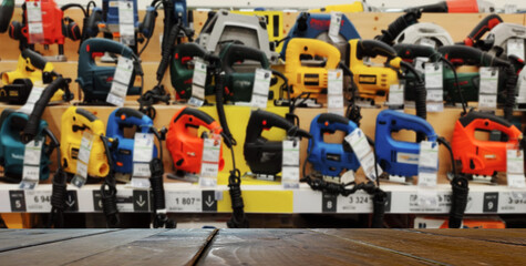 Mock up template, wooden table top, desk top counter in foreground for your product or text. Defocused blurred image of shelves with electric tools. Drills, screwdrivers, jigsaw, saw.