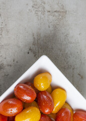 red and yellow small tomatoes in white square bowl on grey background. Flat lay. Recipe idea