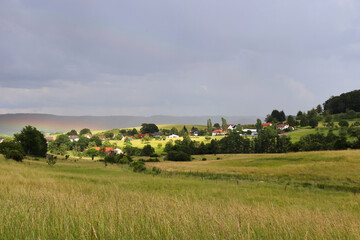 Colorful rainbow over the town of Potzbach, Germany with sun shining on the buildings on a cloudy day.