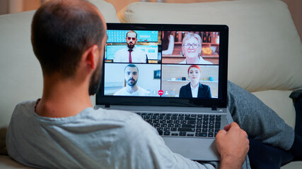 Focused adult using laptop computer during videocall conference talking about social business connection while sitting on couch. Relaxed man working at online communication project overtime in kitchen