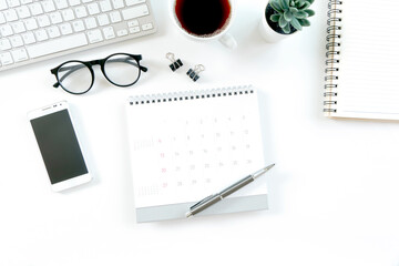 Modern white office desk table with computer, calendar, notebook, tree, glasses and cup of coffee. Top view with copy space,