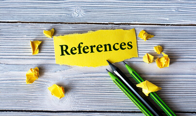 REFERENCES - word on a yellow tattered piece of paper with pencils and crumpled paper lumps on a light wooden background
