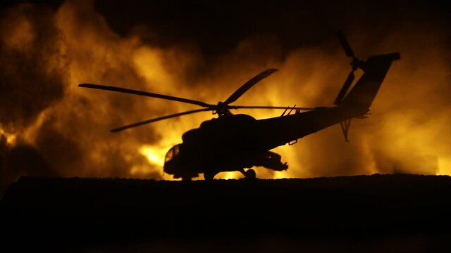Silhouette of military helicopter ready to fly from conflict zone. Decorated night footage with helicopter starting in desert with foggy toned backlit. Selective focus. War concept