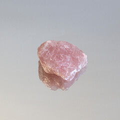 Piece of unpolished pink quartz on white mirror. Minimal color still life Narrow focus line, shallow depth of field