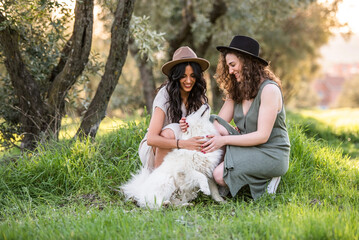 a lesbian couple playing with a white puppy in the field at sunset. lesbian concept