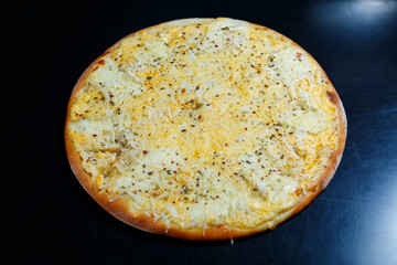 Delicious Four Cheeses pizza with cheddar, parmesan, mozzarella and tomato sauce on a black background. View from above.