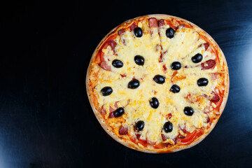 Pizza with cheese tomato sauce, olives, fresh mozzarella, parmesan and basil and meat on a dark background
