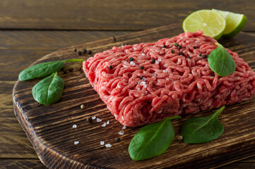 Raw minced beef meat on a wooden cutting board with vegetables and spices. Cooking and healthy eating concept.