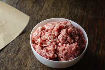 White ceramic bowl with raw minced meat on a dark wooden table.