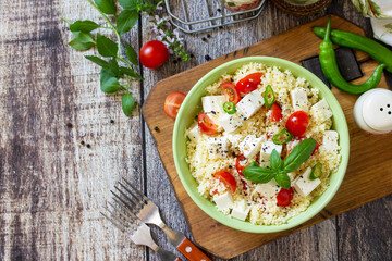 Food dieting concept, tabbouleh salad. Couscous salad with feta cheese, tomatoes, basil and chili on a rustic wooden table. Top view flat lay. Copy space.