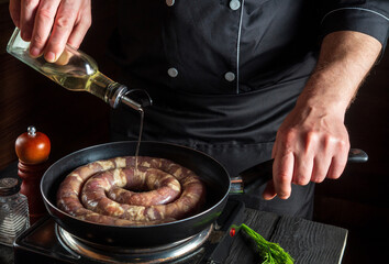 Chef or cook adds oil to pan with raw meat sausage. Preparation for cooking sausages in the kitchen of a restaurant or cafe on a table with vegetables