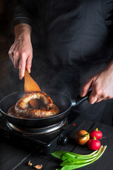 Cooking meat sausage in restaurant kitchen. Chef or cook fries sausage in a frying pan. The idea of a delicious meat diet