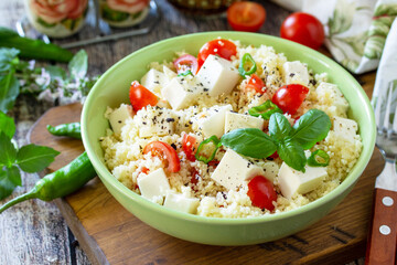 Food dieting concept, tabbouleh salad. Couscous salad with feta cheese, tomatoes, basil and chili on a rustic wooden table.