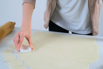 Young woman is cutting circles of dough for cooking dumplings using special form on kitchen at home, hands closeup. Process of cooking dumplings. Minced meat, dough and rolling pin on the table.