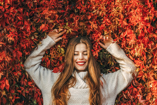 Young happy woman upon a wall of red ivy leaves. She is smiling.