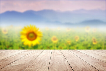 Wooden table top with blurry Sunflower field against mountains landscape