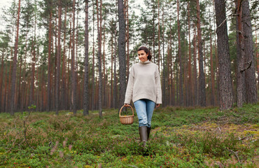 picking season and leisure people concept - young woman with mushrooms in wicker basket walking in forest
