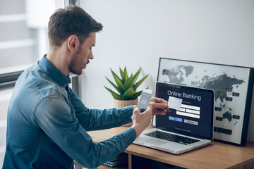 Young man in denim shirt making periodic payments online