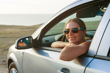 Naklejka premium travel by car. Happy girl with glasses looks out of the car