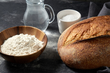 food, baking and cooking concept - homemade craft bread, wheat flour, salt and water in glass jug on table