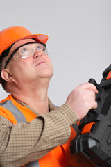 mature construction worker looking up in helmet and eyeglasses lift up tool case on grey background, building working process