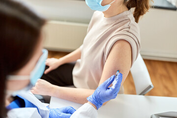 health, medicine and pandemic concept - female doctor or nurse wearing protective medical mask with syringe vaccinating patient at hospital