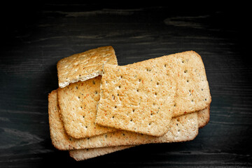 Whole grain cookies, thin crisp bread with spices and herbs on black background.