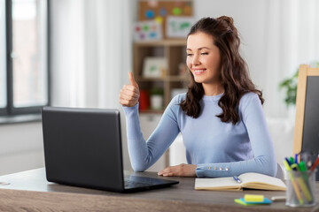distant education, school and people concept - happy smiling female teacher with laptop computer having online class at home showing thumbs up