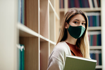 Female college student wearing face mask in library during coronavirus pandemic.