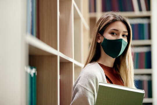 Female College Student Wearing Face Mask In Library During Coronavirus Pandemic.