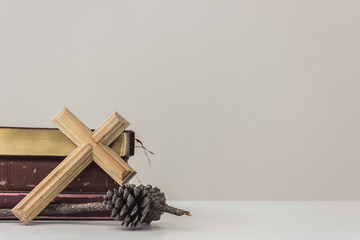 A wooden cross with bible and pine cones.