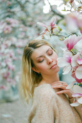 Beautiful young blonde near a blossoming Magnolia tree. Spring.