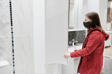 Fototapeta premium Woman chooses a new kitchen for the house. She wears a mask against the virus. Concept of repair, arrangement of apartment and purchase of new furniture for house
