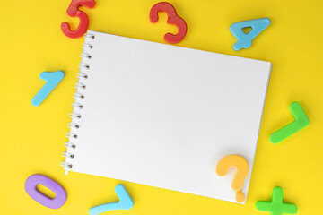 Educational concept. Among the colorful plastic numbers on a yellow background is a notebook with a...