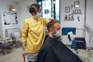 Hairdresser and customer in a salon with medical masks during virus pandemic. Working with safety mask.