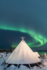 Vertical shot of a traditional tipi in the snowy forest against Northern lights background, Tromso © Eivind Vollset Kristiansen/Wirestock
