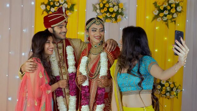 Friends taking selfies with the Indian bride and groom after their Jaimala ceremony. Medium shot of a young boy and girl clicking pictures with friends/relatives - Indian marriage rituals