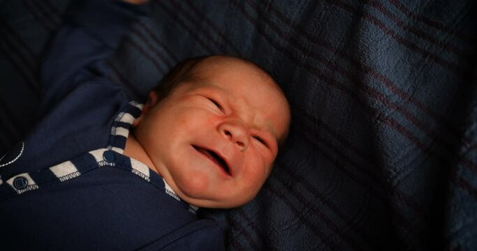 Newborn crying baby boy. New born child tired and hungry in bed under a blue knitted blanket.