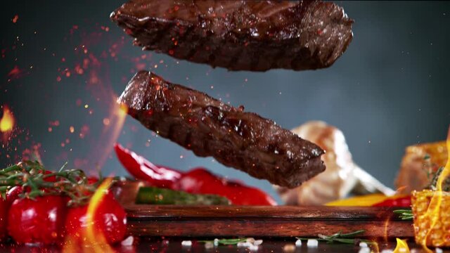 Close-up of Falling Tasty Beef Steaks with Fire Flames, Super Slow Motion